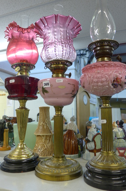 Four 19th century brass column and glass oil lamps including cranberry and coloured glass shades. (S