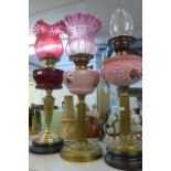 Four 19th century brass column and glass oil lamps including cranberry and coloured glass shades. (S