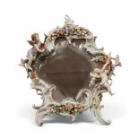 SMALL PORCELAIN MIRROR, EARLY 20TH CENTURY with flowers frame, leaves and figures of cupids. Support