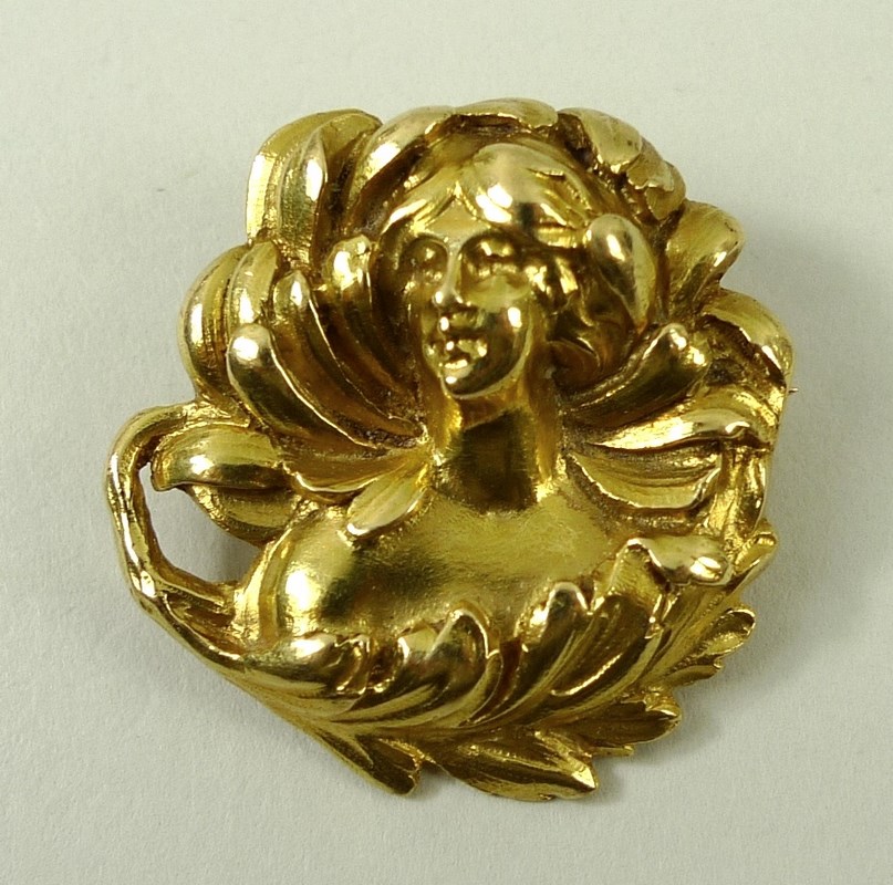 An Art Nouveau yellow metal brooch of circular design with naturalistic swirling adornments to a