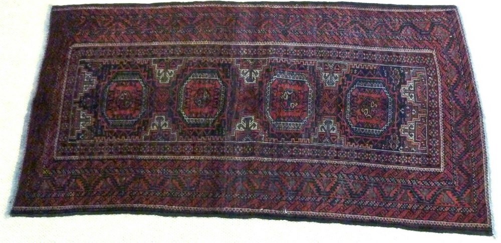 A Baluchi rug with dark red ground, four square medallions with canted corners,