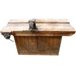 A Victorian pine work bench, with two cast metal clamps attached, cupboard below,