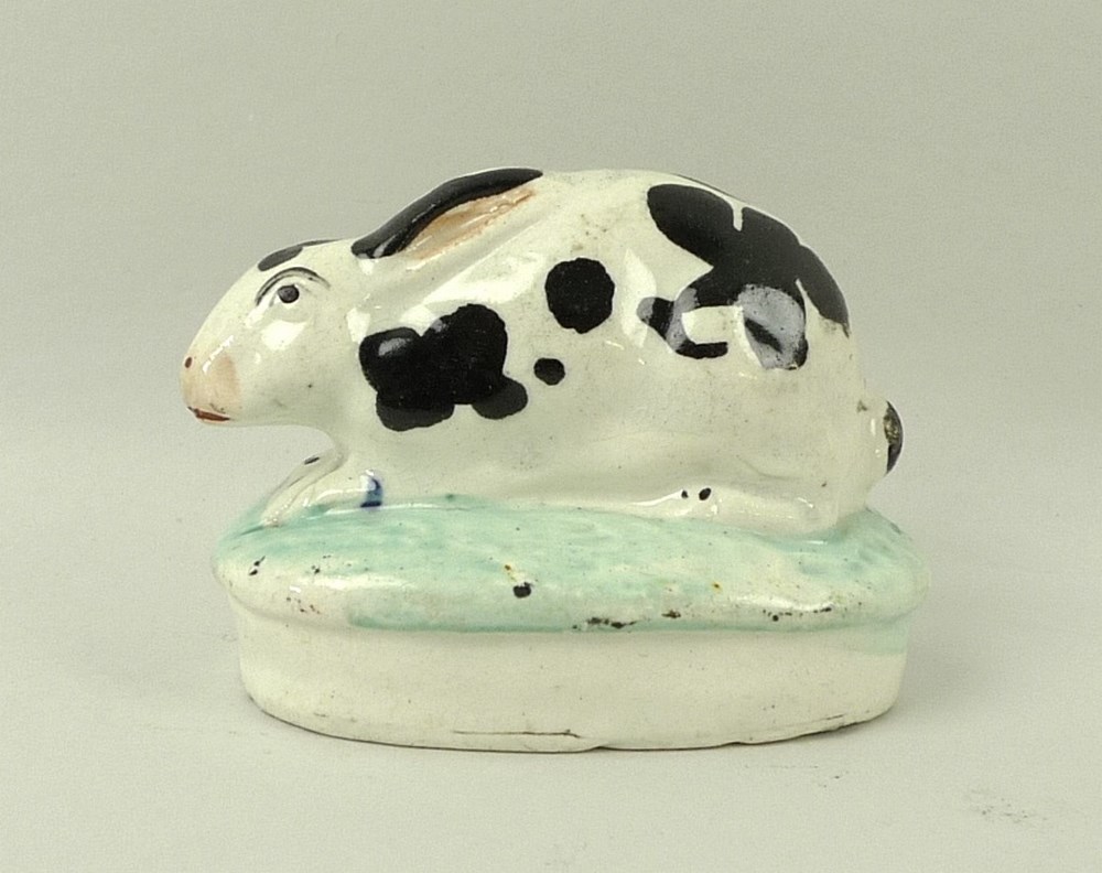 A Staffordshire model of a rabbit, 19th century, on oval base, hand painted black and white,