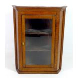 An oak corner cupboard, early 19th century, with single glazed door enclosing two shaped shelves,