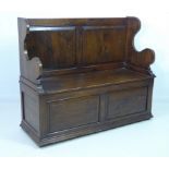 An oak settle, 20th century, with a lift up seat, two panel back and shaped sides,