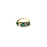 A gold, emerald and diamond set five stone ring, mounted with three cushion shaped emeralds,