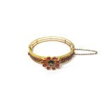 A gold, ruby and diamond set oval hinged bangle, the front with a flowerhead motif,