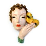 A Goldscheider pottery wall mask, 1930's, depicting an Art Deco female bust holding a yellow mask,