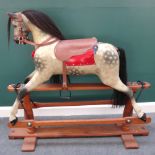 A dapple grey carved wooden rocking horse with leather tack on a swing frame base,