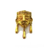 A gold pendant brooch, designed as an Aztec style mask with three pendant drops to the front,