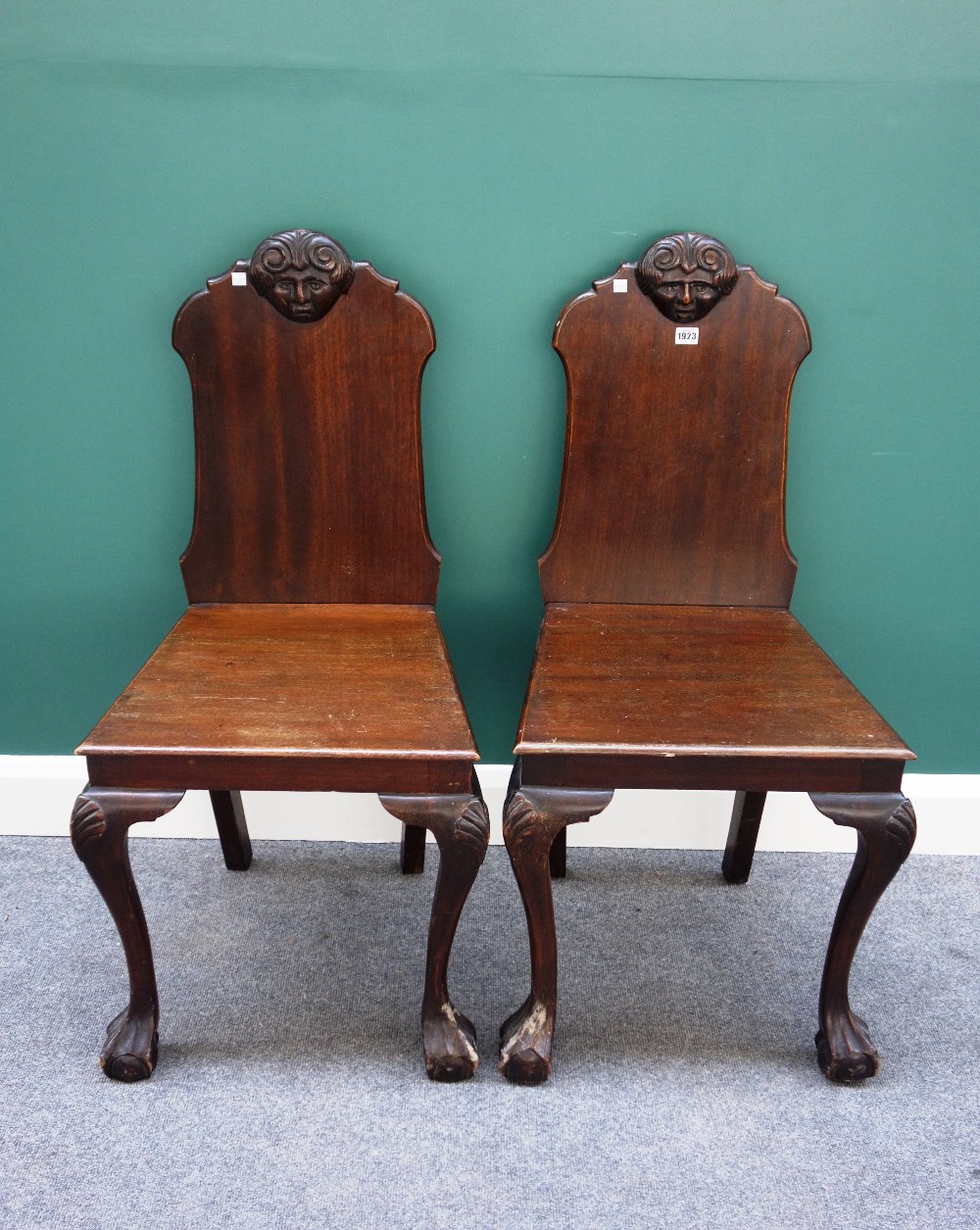 A pair of 19th century mahogany hall chairs, the shaped backs with carved face masks,