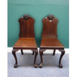 A pair of 19th century mahogany hall chairs, the shaped backs with carved face masks,