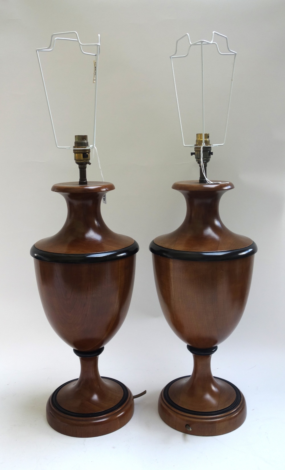 A pair of modern fruitwood table lamps, each of urn form with ebonised banding, on a circular foot,