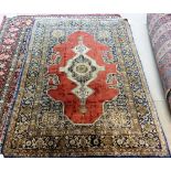 A Ghom silk rug, Persian, the plain madder field with an extended ivory medallion,