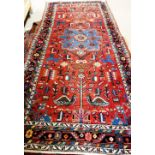 A West Persian rug, the madder field with a bold indigo medallion, pairs of peacocks, flags,