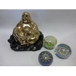 A golden brass Buddha in carved wooden seat, together with three glass paperweights.