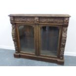 A 19thC carved oak glazed twin door cupboard, the two frieze drawers with Green Man carved handles,