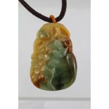 AN ORIENTAL CARVED BI-COLOUR JADE PENDANT on a plaited cord, 40cm long