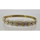 A DIAMOND AND GOLD COLOURED METAL BANGLE the top with twin rows of small diamonds and snap clasp,