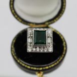 AN EMERALD AND DIAMOND CLUSTER RING having central trap cut emerald bordered by two baguettes,