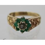 A 1970's 9CT GOLD EMERALD AND DIAMOND CLUSTER RING having floral head with central diamond on cast