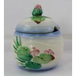 A CLARICE CLIFF JAM POT with cover, having moulded body with hand painted waterlily decoration, with