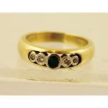 AN EMERALD AND DIAMOND GYPSY SET GOLD COLOURED METAL DRESS RING, having central oval emerald flanked