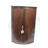 A GEORGE III MAHOGANY BOW FRONT HANGING CORNER CUPBOARD, 67cm wide x 99cm high