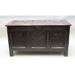 AN 18TH CENTURY OAK COFFER having hinged triple panel lid, carved decoration to the front, raised on