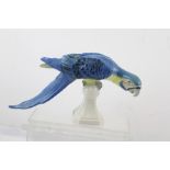 A ROYAL DUX MODEL OF A BLUE MACAW, perched on a stand in typical inquisitive stance, decorated in