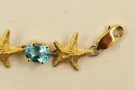 A MODERN GOLD COLOURED METAL BANGLE of alternating five point starfish and oval claw, set blue topaz - Image 3 of 4