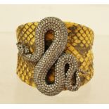 A CONTEMPORARY SNAKESKIN BANGLE spring fitted, mounted with a silver coloured metal and simulated