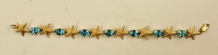 A MODERN GOLD COLOURED METAL BANGLE of alternating five point starfish and oval claw, set blue topaz