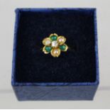 A GOLD COLOURED METAL FLORAL DESIGN DRESS RING, the head set with a brilliant, three emeralds and