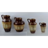 FOUR DOULTON STONEWARE JUGS, decorated in the Egyptian taste with mask spouts and applied slip