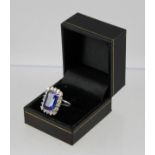 A BLUE TANZANITE & DIAMOND CLUSTER RING, having a trap cut central stone bordered by eighteen