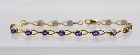 A GOLD COLOURED METAL BRACELET set sixteen oval amethysts in claw mounts