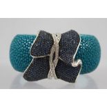 A DESIGNER SILVER COLOURED METAL, BLUE CRYSTAL AND RAY SKIN BANGLE, having bi-colour entwined wrap