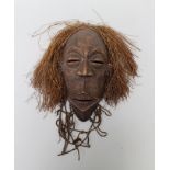 A CARVED WOOD AFRICAN TRIBAL MASK with facial scarification and vegetation hair, originating in