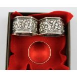 ARTHUR HARRIS A PAIR OF EDWARDIAN SILVER NAPKIN RINGS of hexagonal form with repousse floral