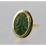 A 14CT GOLD AND JADE RING, with central oval carved jade stone set in stepped mount on plain