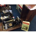 A mounted black, gold decorated sewing machine with mahogany lid and an old sewing machines