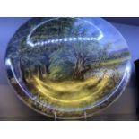 A large painted plate depicting a pastoral river scene, signed and dated 1883.