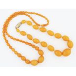 Two strings of graduated amber-coloured plastic beads, one string length approx. 26", the other