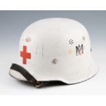 A DRK German Red Cross helmet in white with red cross to front with swastika emblem to side, has
