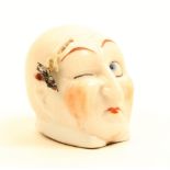 An early 20th Century souvenir porcelain tape measure in the form of a distorted mans head, one