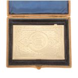 A silver visiting card case in outer leather case, the card case engraved with a belted cartouche to