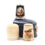 Three thimbles comprising a Worcester style porcelain example painted with a robin and foliage, a