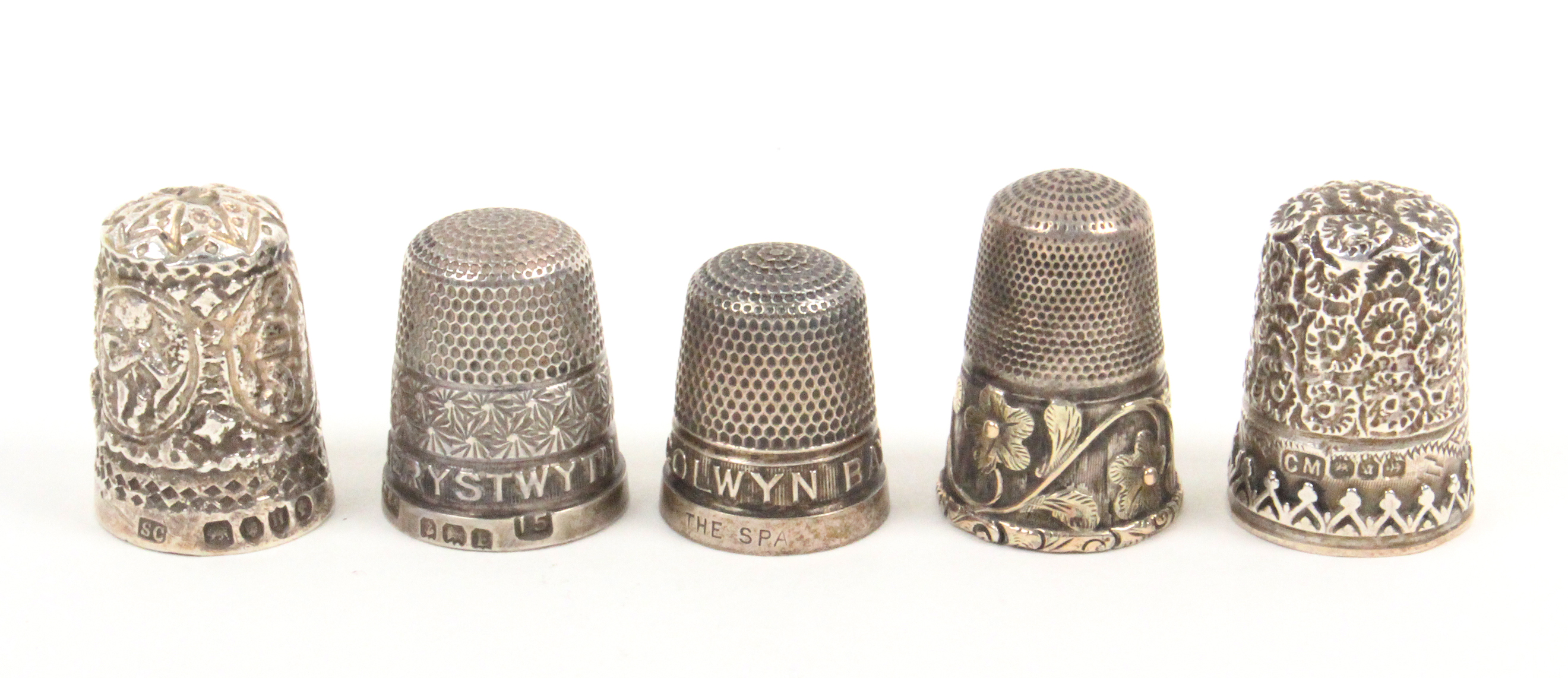 Five English silver thimbles comprising a tall example with two colour floral and leaf scroll