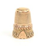 A gold thimble with swirl decorated frieze overlaid with an arrowhead and fleur de lis border,